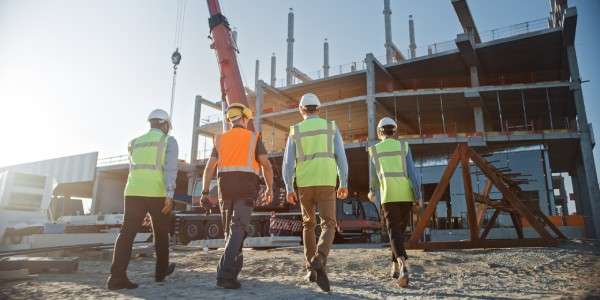 How to Prevent Frozen Pipes 145 Four construction workers are walking through a construction site. There is a tall crane and a large building on site.