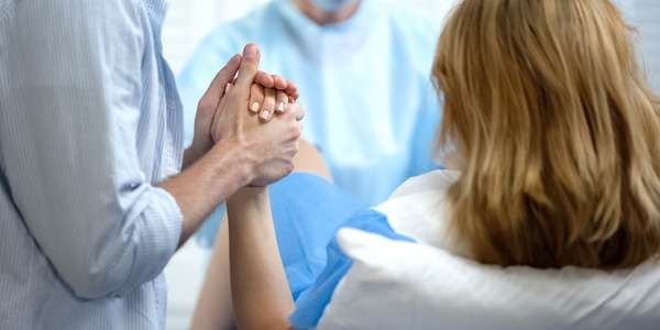 Dance Your Stress Away: The Wellness Benefits of Belly Dance for All Ages 38 A person wearing a blue striped button-down holds the hand of a woman who's lying in a hospital bed giving birth.