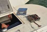 A close-up of a boat floating in some water. A door is open to the boat's motor with tools on the deck.